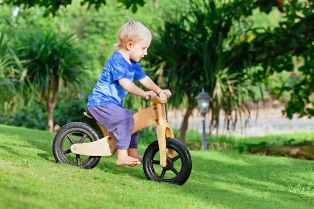 Un petit garçon jouant avec sa draisienne en bois dans le jardin