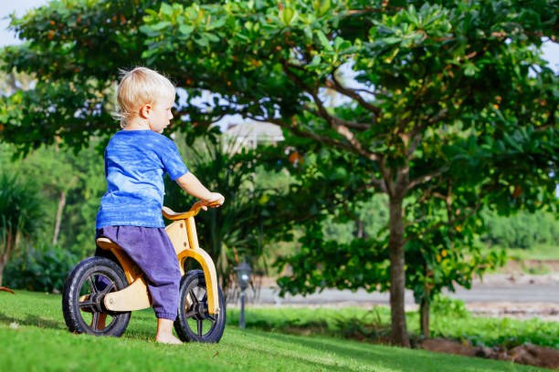 Garçon joyeux de 2 à 3 ans sur une draisienne en bois Enfant heureux, pieds nus, apprenant à rouler et à garder l'équilibre sur un vélo d'entraînement dans le jardin.