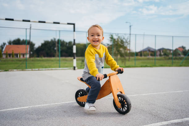 Un jeune garçon enjoué sur une draisienne en bois sur un terrain de sport.