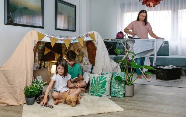Mother ironing while her children play camping at home in the living room Un exemple de lit tipi Montessori