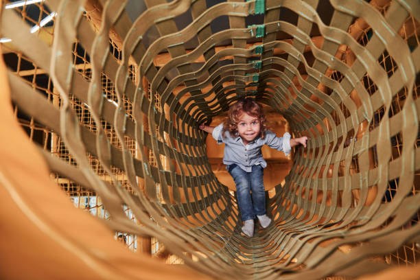 Exercice de motricité : l'enfant s'amuse dans la salle de jeux en traversant la cage en bois.