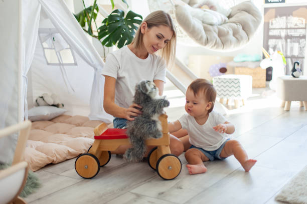 Une jeune mère mignonne et sa petite fille jouent dans la salle de jeux avec un petit vélo en bois de style d'une draisienne