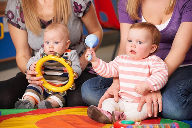 Learning and having fun Deux bébés avec ses mamans jouant à des hochets sur un tapis de motricité
