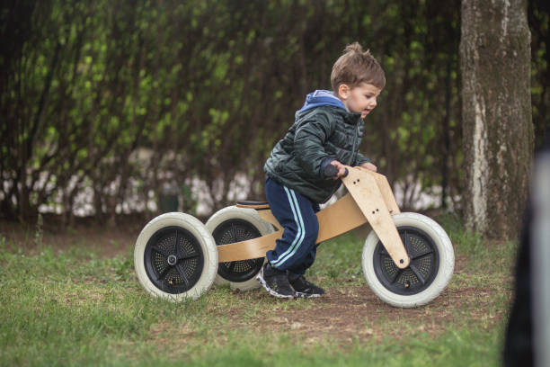 Jeune garçon faisant du vélo de type draisienne en bois, par une belle journée de printemps dans le jardin.