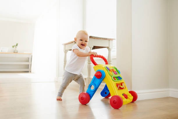 Portrait of an adorable baby girl playing with a toy walker at home Un bébé très souriant jouant avec son joli chariot