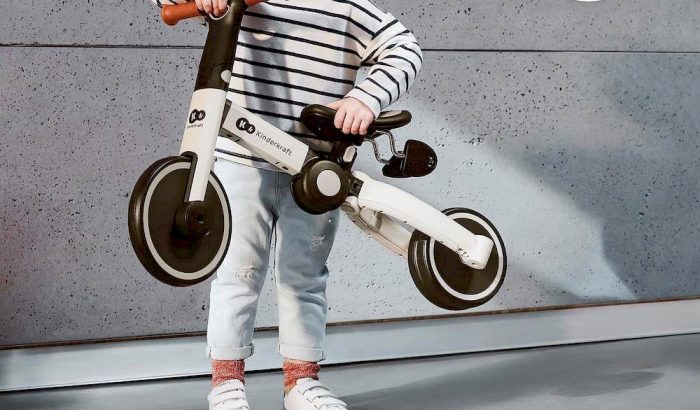 Un enfant tenant un tricycle Kinderkraft